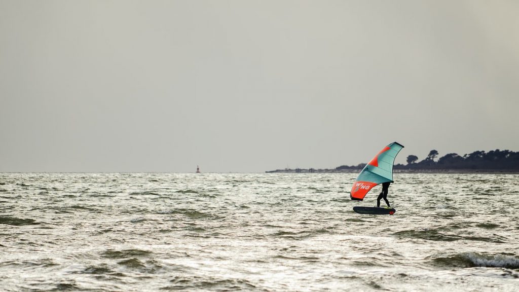 Wing surfer in actie met opblaasbare wing en foilboard op het water